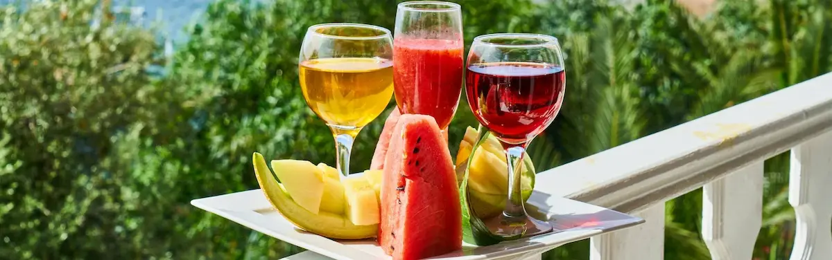 Frische Wassermelonen- und Melonenstücke neben farbenfrohen Fruchtsäften und Smoothies auf einem weißen Teller; ein inspirierendes Beispiel für unsere Themenwelten: Ihr Kompass für ein gesundes Leben.
